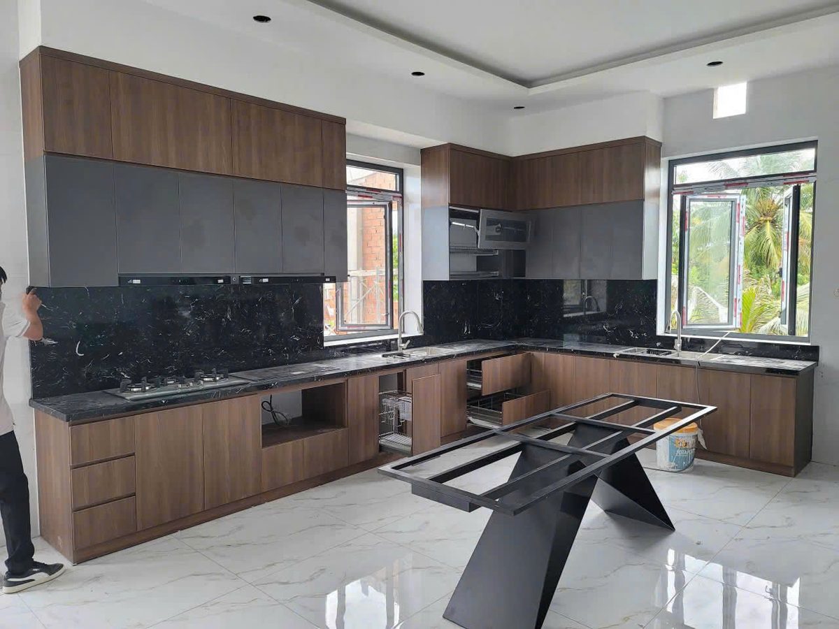 Tủ bếp chữ L gỗ vân óc chó phối mặt đá granite đen, cạnh cửa sổ lấy sáng - Nội Thất Hà Tuấn LX