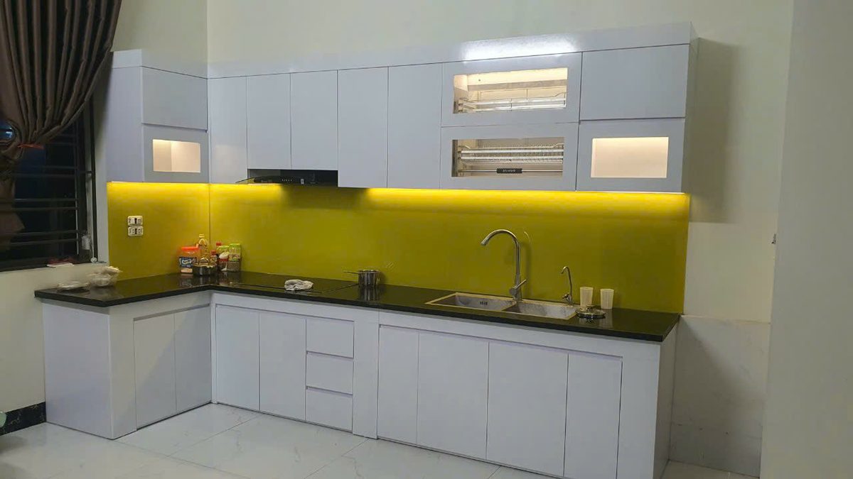 Tủ bếp chữ L cánh trắng, kính ốp bếp màu vàng nổi bật, sạch sẽ hiện đại - Nội Thất Hà Tuấn LX